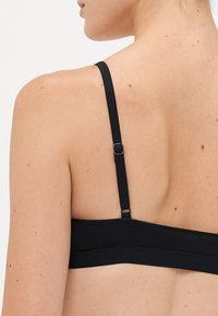 Woman's upper back with black adjustable bra strap and clasp visible on light skin with freckles and moles.