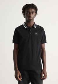 Camiseta polo negra con un cuello a rayas, mangas cortas y un pequeño parche con logo en el pecho. Fabricada con una tela suave y transpirable.
