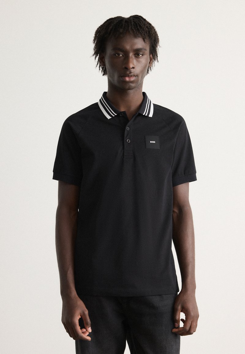 Camiseta polo negra con un cuello a rayas, mangas cortas y un pequeño parche con logo en el pecho. Fabricada con una tela suave y transpirable.