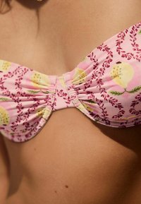 Top bikini rosa con un motivo floreale che presenta pere gialle e piccole foglie. Tessuto arricciato al centro e texture liscia.