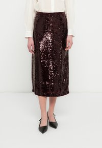 Jupe midi en sequins bordeaux à la silhouette ajustée, avec des fentes latérales et une texture brillante, associée à des talons noirs à bouts pointus.