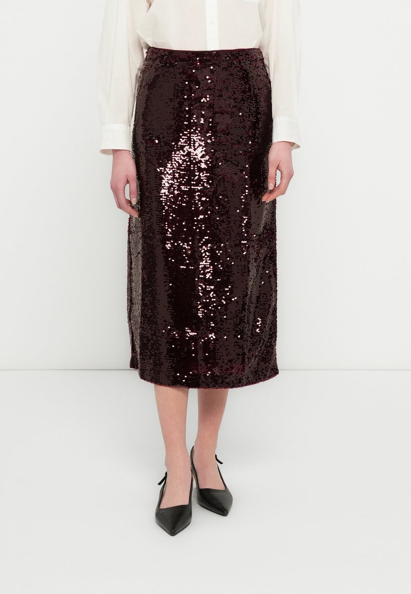 Jupe midi en sequins bordeaux à la silhouette ajustée, avec des fentes latérales et une texture brillante, associée à des talons noirs à bouts pointus.