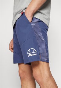 Navy blue athletic shorts in lightweight material, featuring a white logo, side pockets, and a geometric pattern on the side panels.