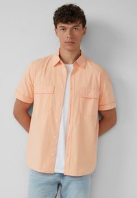 Korte mouwen, button-up shirt in pastel perzik met een gestructureerde afwerking, voorzien van twee borstzakken en opgerolde mouwen. Draag het over een wit T-shirt.