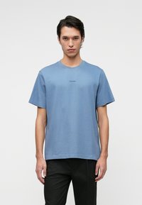 Világoskék pamut póló rövid ujjakkal és kerek nyakkivágással. Elől egy kis fekete "Calvin Klein" logó található.