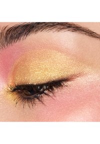 Close-up of an eye featuring golden eyeshadow with a shimmery finish, pink blush, and defined black eyelashes, against a smooth skin background.