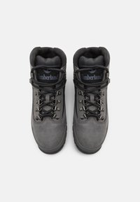 Pilkai atsparūs vandeniui žygio batai su aukšta dizaino forma, su apvaliais raišteliais, metalinėmis akytėmis ir paminkštintais apykaklėmis komfortui. Matomas Timberland logotipas.