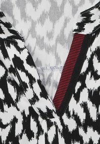 Černobílý top s cikcak vzorem, s akcentem červeného a černého pruhu na límci. Měkká tkanina, design s výstřihem do V a detailním prošíváním.