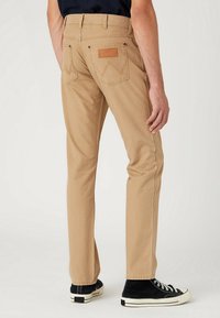 Pantalones de algodón beige con diseño de pierna recta, que cuentan con dos bolsillos traseros, costuras visibles y un parche de cuero en la cinturilla.