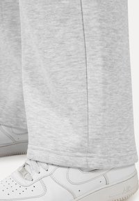 Pantalones de chándal gris claro con una textura suave y un diseño ligeramente ajustado, combinados con zapatillas blancas que presentan perforaciones y detalles de logo.