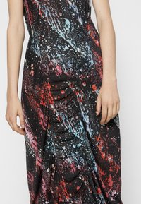 Close-up af en kvinde iført en sort kjole med malerprikker i rød, blå og pink samt subtile rynkedetaljer.