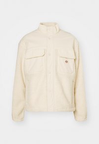 Giacca in fleece di colore crema con parte superiore in tessuto liscio e parte inferiore in sherpa testurizzato. Presenta due tasche sul petto e una chiusura frontale con bottoni a pressione.