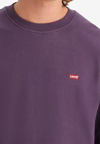 Sweat-shirt violet en coton, avec un col rond, des manches longues, et une petite étiquette rouge du logo Levi's sur la poitrine.
