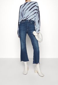 Light blue tie-dye long-sleeve top, high-waisted blue jeans with flared hem, and white heeled boots. The bag is white and knotted.