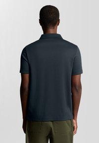 Mörk marinblå polo med mjukt tyg, klassisk krage och korta ärmar, med en ren baksida.