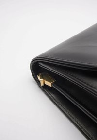 Borsa a mano nera in pelle con design piegato, dotata di una chiusura in tono oro e dettagli del marchio in rilievo all'interno. Texture liscia con linee pulite.