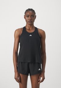 Tricou sport negru fără mâneci, cu design racerback și logo alb Adidas pe piept. Asortat cu pantaloni scurți negri cu logo-ul Adidas. Textură fină.