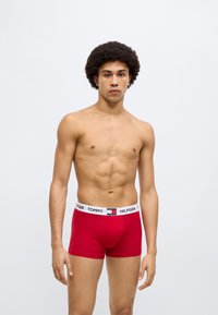 Κόκκινα βαμβακερά μπόξερ με άσπλη ελαστική ζώνη μέσης διακοσμημένη με λογότυπο. Ο σχεδιασμός είναι εφαρμοστός και λείος, χωρίς επιπλέον σχέδια.