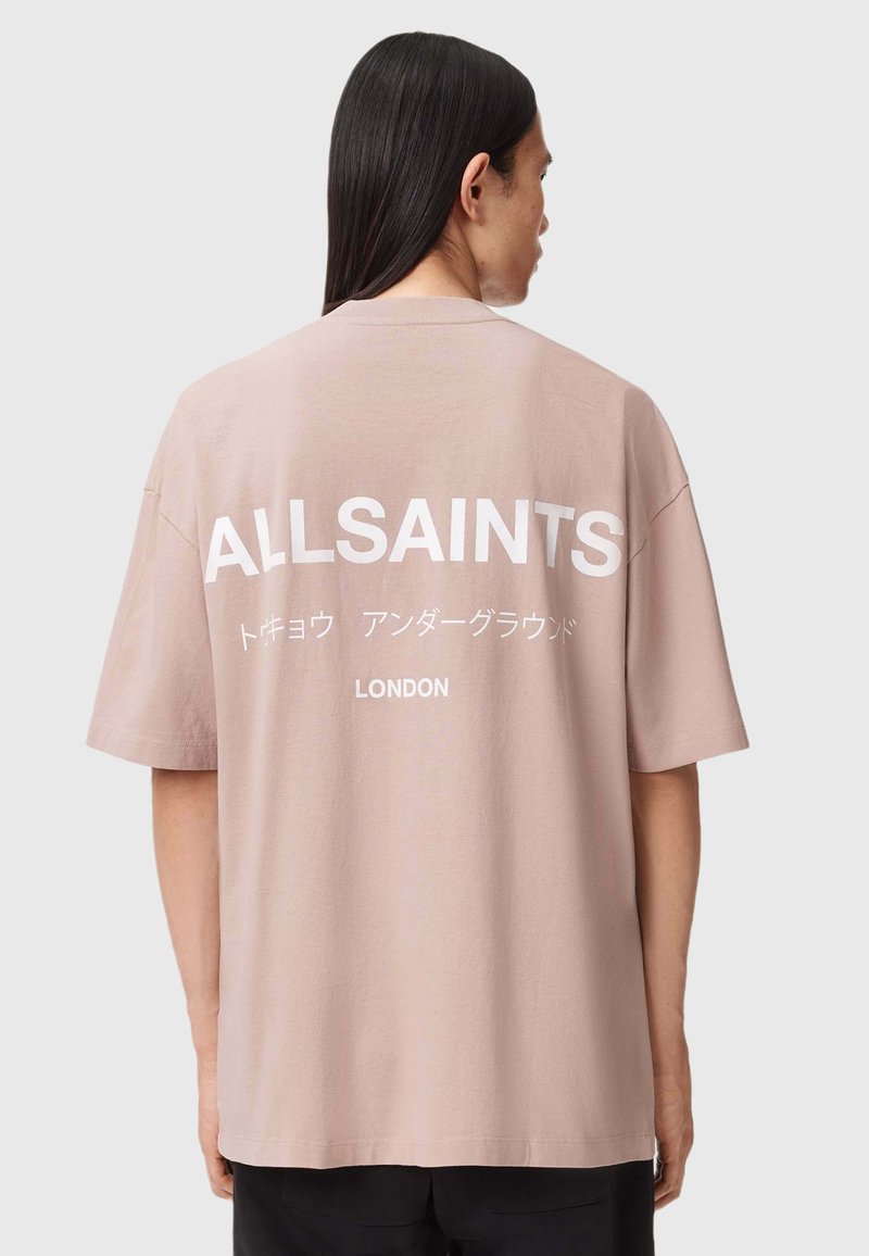 Helles rosa T-Shirt mit kurzen Ärmeln und großen weißen Schriftzügen "ALLSAINTS" und "LONDON" auf dem Rücken. Weicher Stoff mit einem entspannten Schnitt.