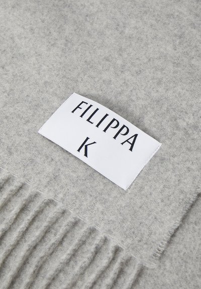 Šedý šátek s texturovaným povrchem. Má třásně a bílou štítek s označením "FILIPPA K" v černém písmu.