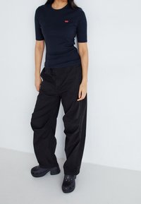 Granatowy t-shirt z krótkim rękawem z czerwonym logo, zestawiony z luźnymi czarnymi spodniami i czarnymi klapkami z dziurkami i małym obcasem.