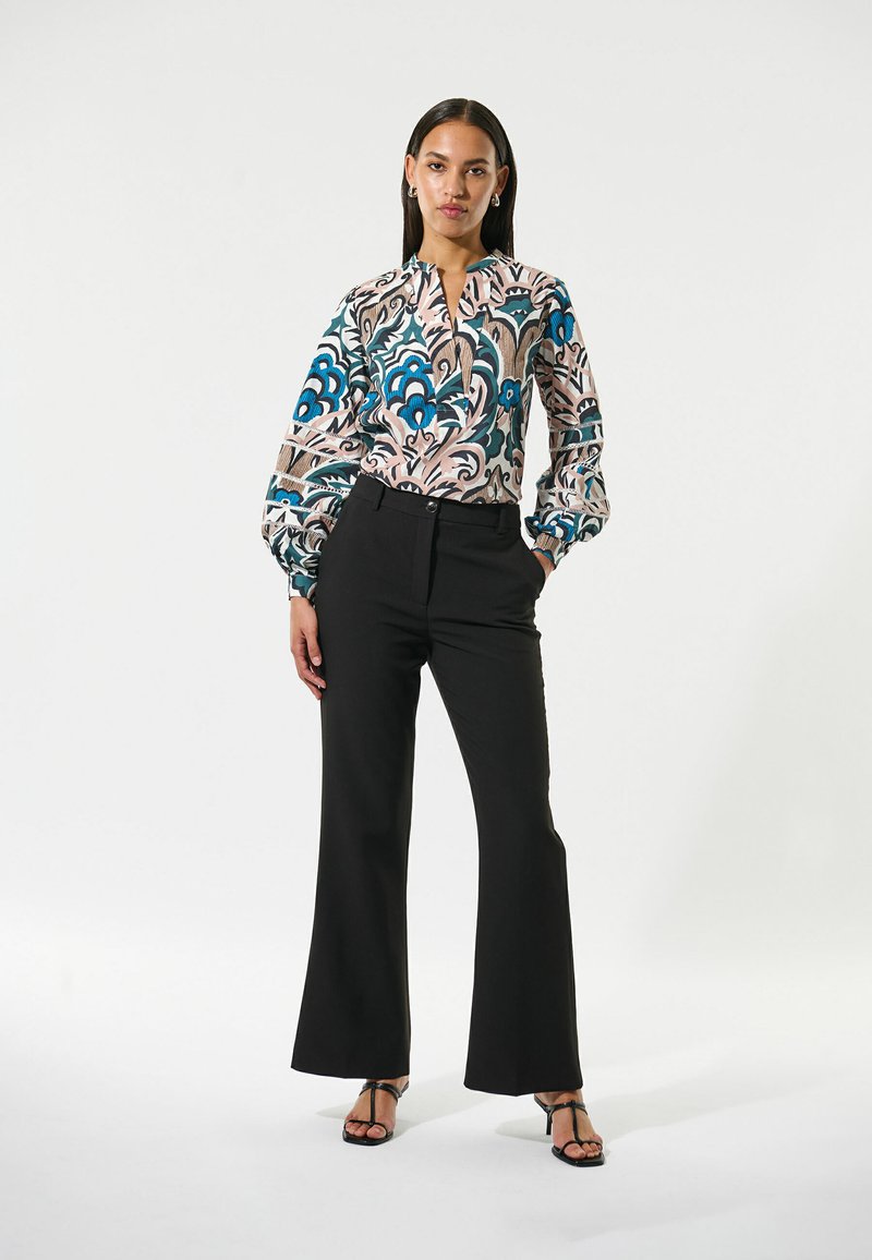 Bedruckte Bluse mit blauem und pinkem Blumenmuster, langen Puffärmeln, kombiniert mit schwarzen weit geschnittenen Hosen und schwarzen Riemchensandalen.