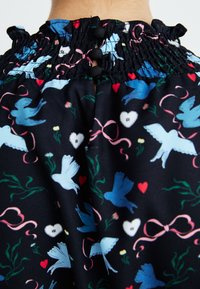 Top de tecido preto com decote franzido, adornado com um padrão colorido de pássaros, corações, flores e fitas. Detalhe de três botões nas costas.