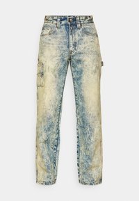 Løse cargo-bukser i falmet blå denim, med multiple lommer, synlig søm, og en slitt tekstur med lette folder.