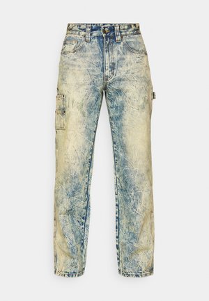 Løse cargo-bukser i falmet blå denim, med multiple lommer, synlig søm, og en slitt tekstur med lette folder.