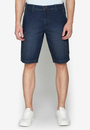 Mørke denim shorts med lige snit, der har sidelommer, syninger og knaplukning, parret med hvide sneakers.