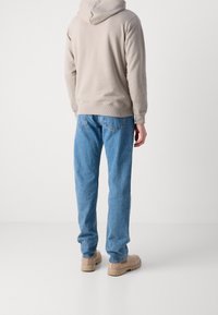 Sudadera beige con capucha, jeans azules y botas color beige. La sudadera tiene un dobladillo acanalado, y los jeans tienen un corte relajado con bolsillos traseros.
