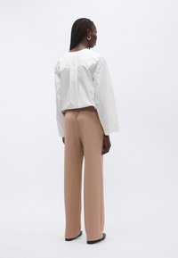 Λευκό τοπ με μακριά μανίκια, στρογγυλή λαιμόκοψη και άνετη γραμμή, συνδυασμένο με μπεζ παντελόνι με φαρδιά πόδια και μαύρα παπούτσια. Ομαλή υφή υφάσματος.