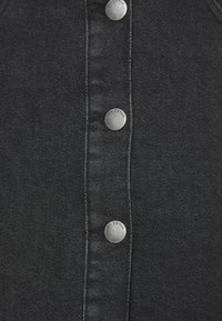 Černá denimová látka má přední zapínání na knoflíky s kovovými stříbrnými knoflíky s nápisem "J.D. Denim". Hladký povrch a tmavá barva.