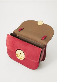 Borsa a tracolla compatta realizzata in suede rosso e pelle liscia. Presenta una chiusura rotonda oro e un interno in tessuto marrone con una tasca con zip.