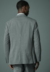 Chaqueta de traje gris con rayas, con solapa muesca, hombros estructurados y una abertura en la parte posterior. Tejido texturizado con un brillo sutil.