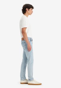 White short-sleeve t-shirt, light blue jeans, and cream sneakers with gum soles. Side profile view against a plain white background.