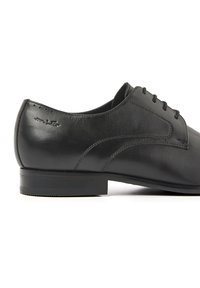 Zwarte leren veterschoen met een gladde afwerking, ronde neus en een lage, platte hak. Heeft gestikte details langs de zijkanten.