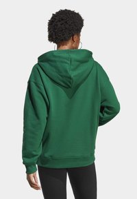 Grön huvtröja med avslappnad passform, som har dragsko i huvan, uppvikta ärmar och en strukturerad tygkvalitet. Enfärgad design, inga mönster.