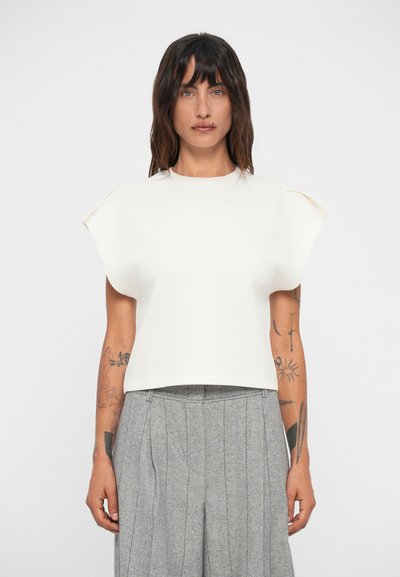 Weißes, kurzes Top mit kurzen, strukturierten Ärmeln. Glatte Textur; schlichtes Design. Kombiniert mit grauen, plissierten Hosen.