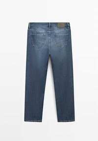 Pohled zezadu na modré džínové kalhoty se dvěma zadními kapsami, poutky na opasek a hnědou koženou značkou na pasu.