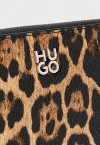 Læderpung i leopardprint i tekstureret brun og sort materiale, med et metallic sølv "HUGO" logo på forsiden. Kompakt og stilfuldt design.