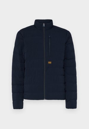 Veste légère matelassée bleu marine avec un col haut, fermeture éclair à l'avant, et un design matelassé horizontal ; dotée d'une poche poitrine et d'un patch logo.
