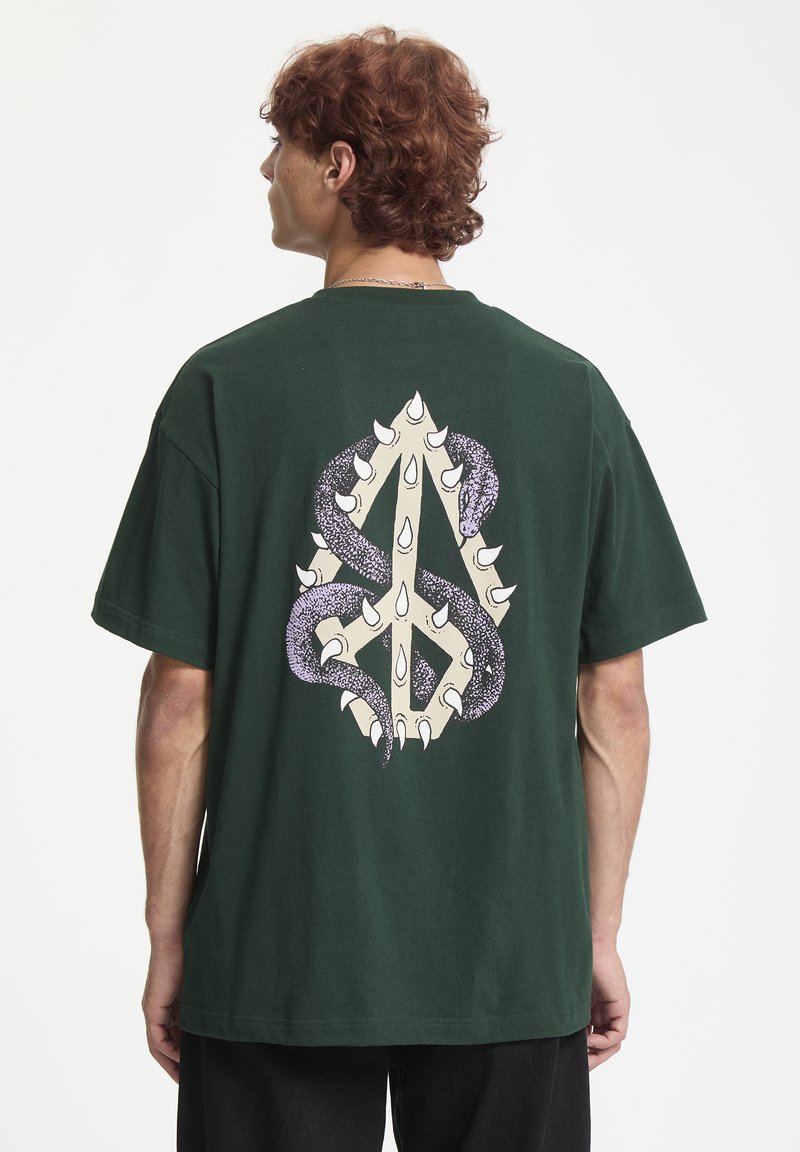 Grøn bomulds T-shirt med et stort design på bagsiden, der viser en beige klo og lilla slangemønstre, korte ærmer og en afslappet pasform.