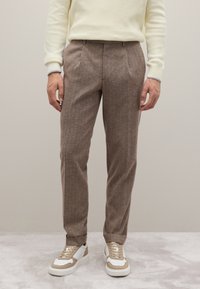 Bruine, gestructureerde broek met een op maat gemaakte snit, voorzien van voorplooien en een rechte pasvorm, gecombineerd met beige en witte sneakers.