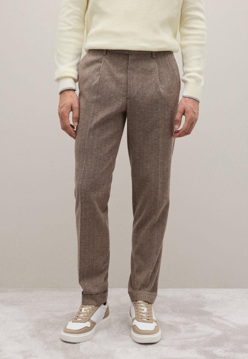 Bruine, gestructureerde broek met een op maat gemaakte snit, voorzien van voorplooien en een rechte pasvorm, gecombineerd met beige en witte sneakers.