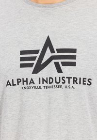 Γκρι βαμβακερό T-shirt με μαύρο γραφικό λογότυπο με γωνιακό σχέδιο και το κείμενο "ALPHA INDUSTRIES" και "KNOXVILLE, TENNESSEE, U.S.A."