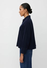 Camicia blu navy con colletto, a bottoni, dal taglio relaxed e maniche lunghe, realizzata in un tessuto morbido. Presenta un orlo curvo e spacchi laterali.