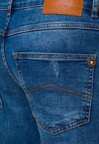 Modré džíny z denimu s jemně vrásčitým povrchem, měděným prošíváním a koženou nášivkou na pasu, s designem zadní kapsy.