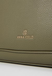 Zielono-oliwkowa torebka z fakturowanej sztucznej skóry z złotym logo "ANNA FIELD". Posiada gładki, ustrukturyzowany kształt z delikatnymi detalami ściegów.