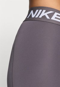 Legginsy damskie Nike z wysokim stanem, wyróżniające się wyraźnym białym logo, gładkim szarym materiałem oraz płaskimi szwami dla zwiększenia komfortu.